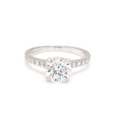 a white gold engagement ring with diamonds on the band and a round brilliant cut diamond in the center