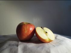 two apples sitting side by side on a white tablecloth with one cut in half