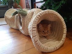 a cat sitting in a crocheted tunnel on the floor next to a christmas tree