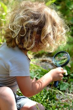 a little boy holding a magnifying glass in his hand while sitting on the ground