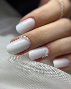 a woman's hand with white nail polish and crystal beads on it, holding onto a