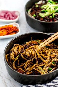 two pans filled with noodles and vegetables on a white tablecloth next to bowls of food