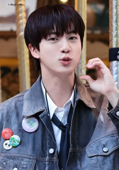 a young man in a denim jacket and tie with buttons on his lapel collar