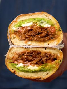 two sandwiches with meat and guacamole are held in one hand while the other is half eaten