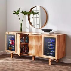 a wooden sideboard with two wine bottles and a plant in it next to a round mirror on the wall