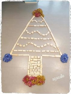 a christmas tree made out of popsicle sticks with flowers on the bottom and blue pom poms around it