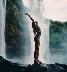 a woman standing in front of a waterfall with her arms up and legs spread out