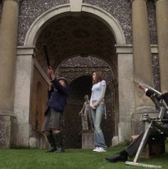 two people standing in front of an arch with statues on the ground and one person holding a baseball bat