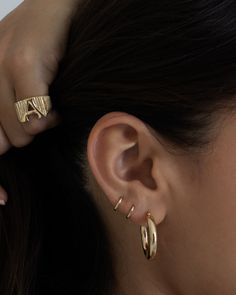 a close up of a person wearing gold earring and an ear cuff with two rings on their ears