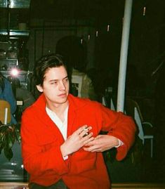 a young man in a red jacket sitting at a table with his hands folded out