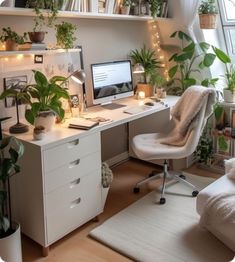 a white desk topped with a computer and lots of plants