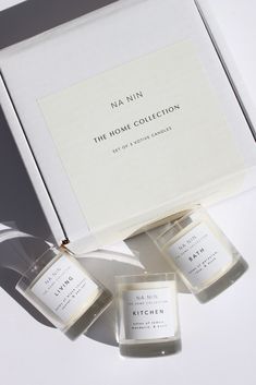 the home collection includes three small candles and an open box with white labels on it