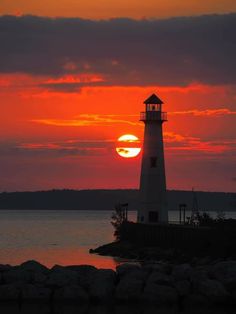 the sun is setting behind a lighthouse on the water