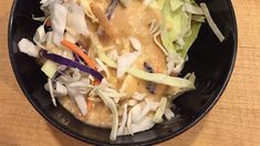 a black bowl filled with salad on top of a wooden table