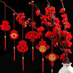 a white vase filled with red flowers next to chinese paper cutouts and string decorations