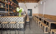 an empty restaurant with wooden tables and benches in front of the bar, along with shelves full of liquor bottles