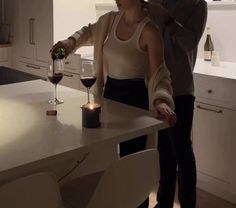 a man and woman standing in a kitchen next to a counter with a glass of wine