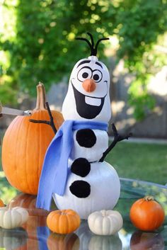 a frosty snowman sitting on top of a glass table next to pumpkins