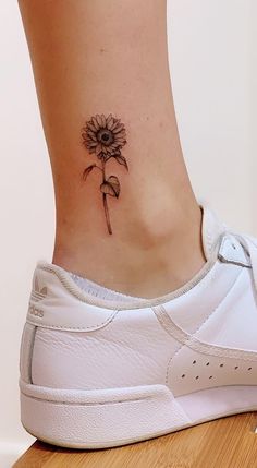 a woman's foot with a flower tattoo on the side of her ankle and behind her is a white tennis shoe