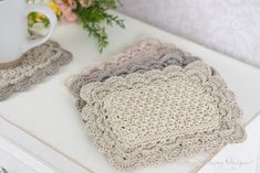 two crocheted coasters sitting on top of a table next to a coffee cup