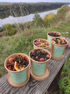 four cups filled with different types of food on top of a wooden table next to a body of water