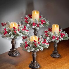 four candles are sitting on a table with holly and red berries