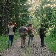 three people walking down a dirt road in the woods with backpacks on their backs