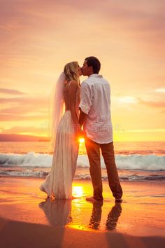 a bride and groom kissing on the beach at sunset