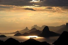 the sun is setting over an island with mountains in the foreground and a boat on the water