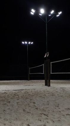 an empty volleyball court at night with some lights on the post and net in the sand