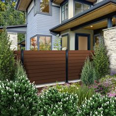 a house that is next to some bushes and flowers in front of the fenced yard