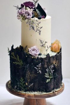 a three tiered cake decorated with flowers and leaves on a wooden stand in front of a white wall