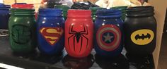 there are many different colored mason jars on the counter together, and one has a spiderman logo