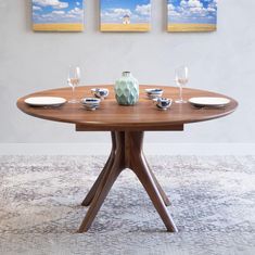 a dining room table with plates and glasses on it in front of three paintings hanging on the wall