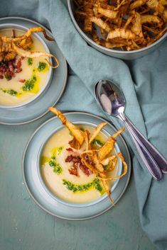 two plates with food on them next to a bowl of french fries and a spoon