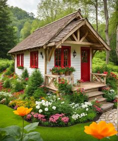 a small white house with red shutters and flowers in the front yard, surrounded by greenery