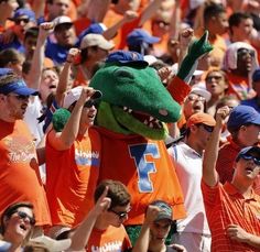 a group of people in orange shirts and blue hats are wearing an alligator costume while holding up their hands