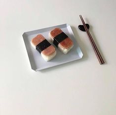 two pieces of sushi on a white plate with chopsticks next to it