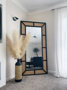 a large mirror sitting on top of a wooden table next to a vase filled with dry grass