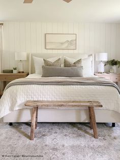 a bedroom with a white bed and wooden bench in front of the bed, along with two lamps on either side of the bed