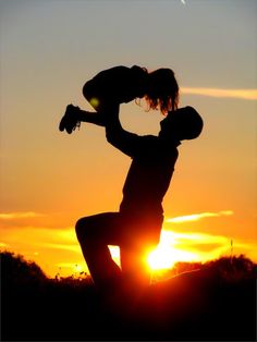 the silhouette of a person holding a child in their arms as the sun sets behind them