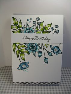 a birthday card with blue flowers and green leaves on the front, sitting on a checkered tablecloth