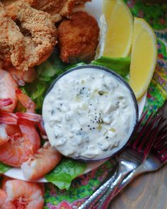 a plate with shrimp, lettuce and sauce on it next to lemon wedges