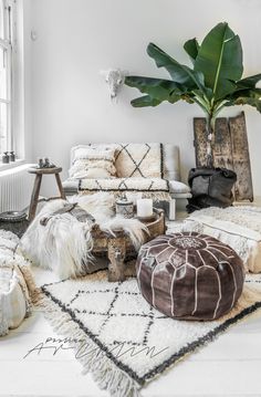 a living room filled with lots of white furniture and plants on the floor next to a window