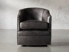 a black leather chair with studded arms and foot rests on the floor in front of a concrete wall