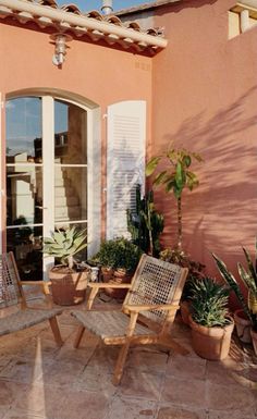 a patio with chairs and potted plants on the side of it, next to an open door