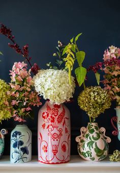 four vases with flowers in them sitting on a shelf next to other vases