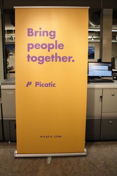 a sign that says bring people together in front of an office cubicle with computers