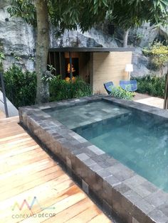 an empty swimming pool in the middle of a wooden decked area with chairs and trees