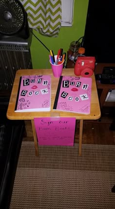 two pink notebooks sitting on top of a wooden table in front of a green wall